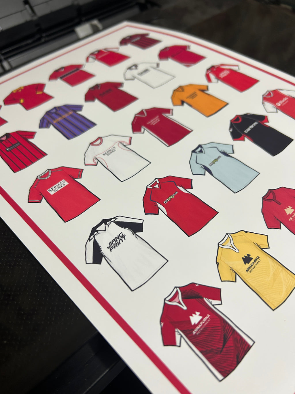 Poster artwork inspired by Morecambe FC shirts, featuring a stylized design with bold red and white color elements. The piece incorporates vintage jersey patterns and textures, capturing the proud tradition and rich heritage of Morecambe Football Club. It blends classic elements with a sharp, contemporary aesthetic that celebrates the enduring spirit of the Shrimps and the club’s historic legacy at the Mazuma Stadium